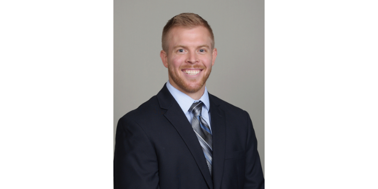 Garrett Gilbert smiles in a black suite in front of a gray background. 